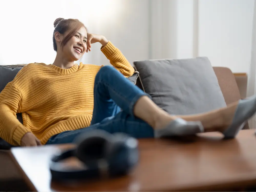 Mulher sorrindo em casa sentada no sofá, transmitindo serenidade e o prazer da própria companhia.