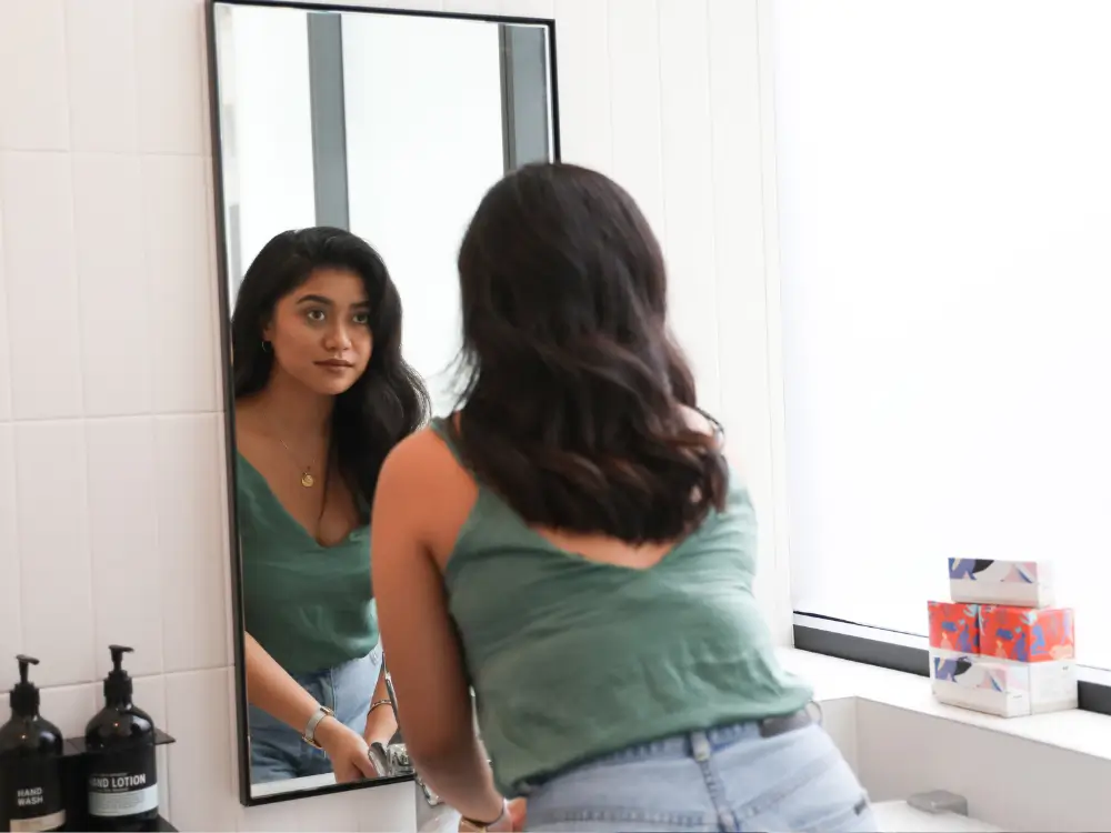 Mulher madura se olhando com carinho no espelho, simbolizando reencontro e amor próprio.”